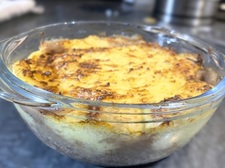 Golden-brown cottage pie topped with creamy mashed potatoes in a glass baking dish